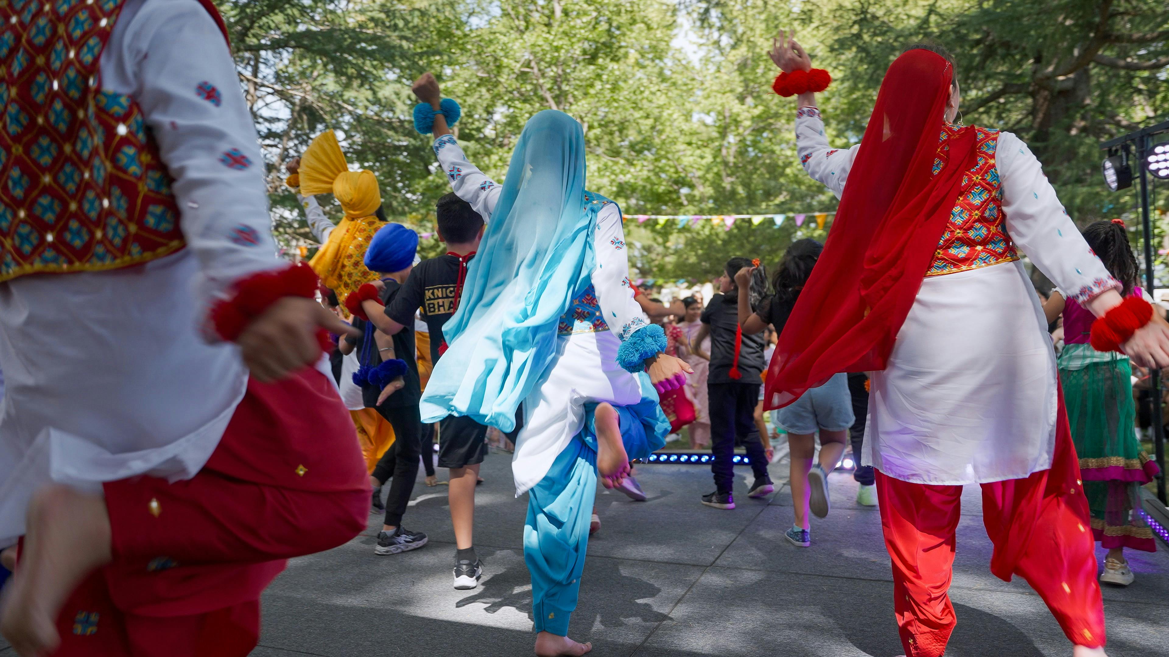 Photo from behind of sevreal dancers on stage in colourful costume
