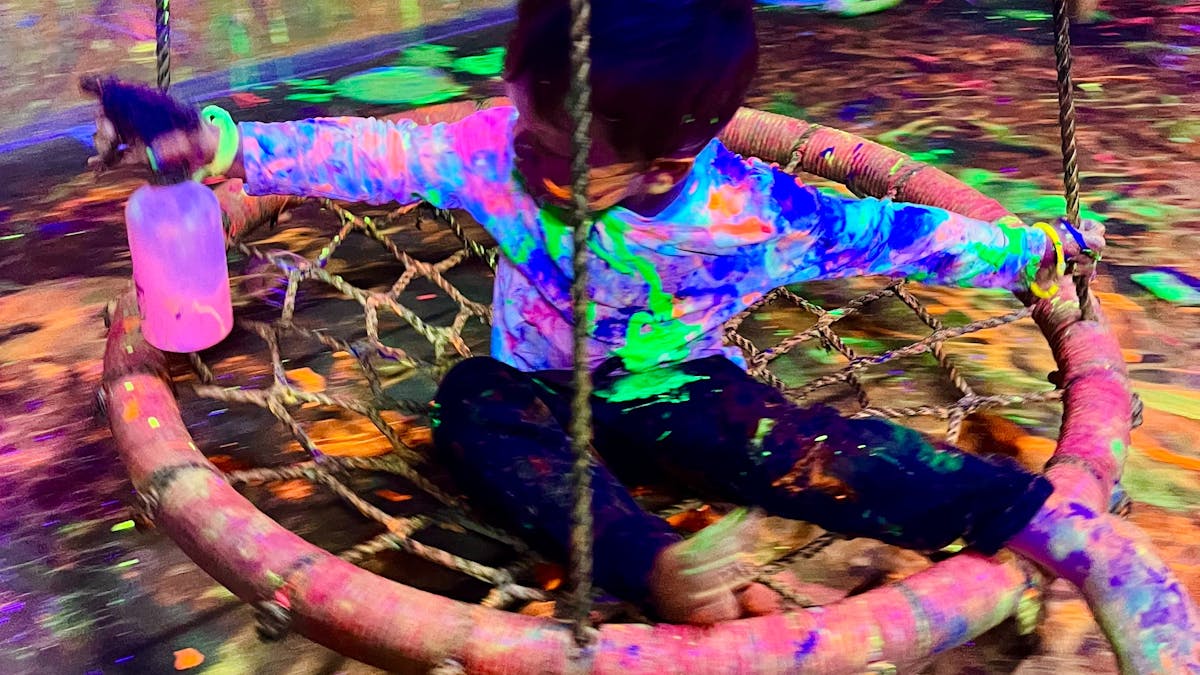 A child swinging on a round swing with a spray bottle at Messy Glow Co