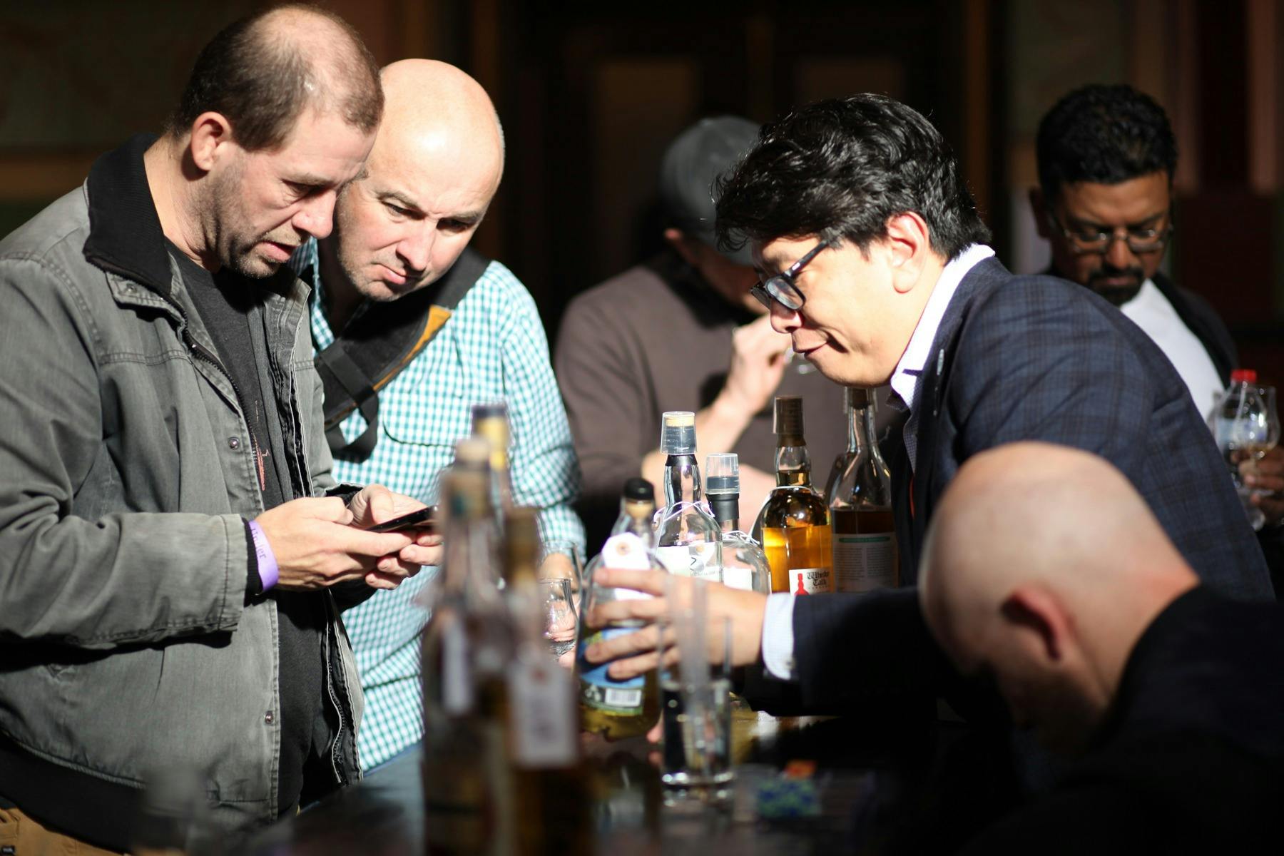 Two men inspect the label of a rare whisky, which is held by a suited staff member.