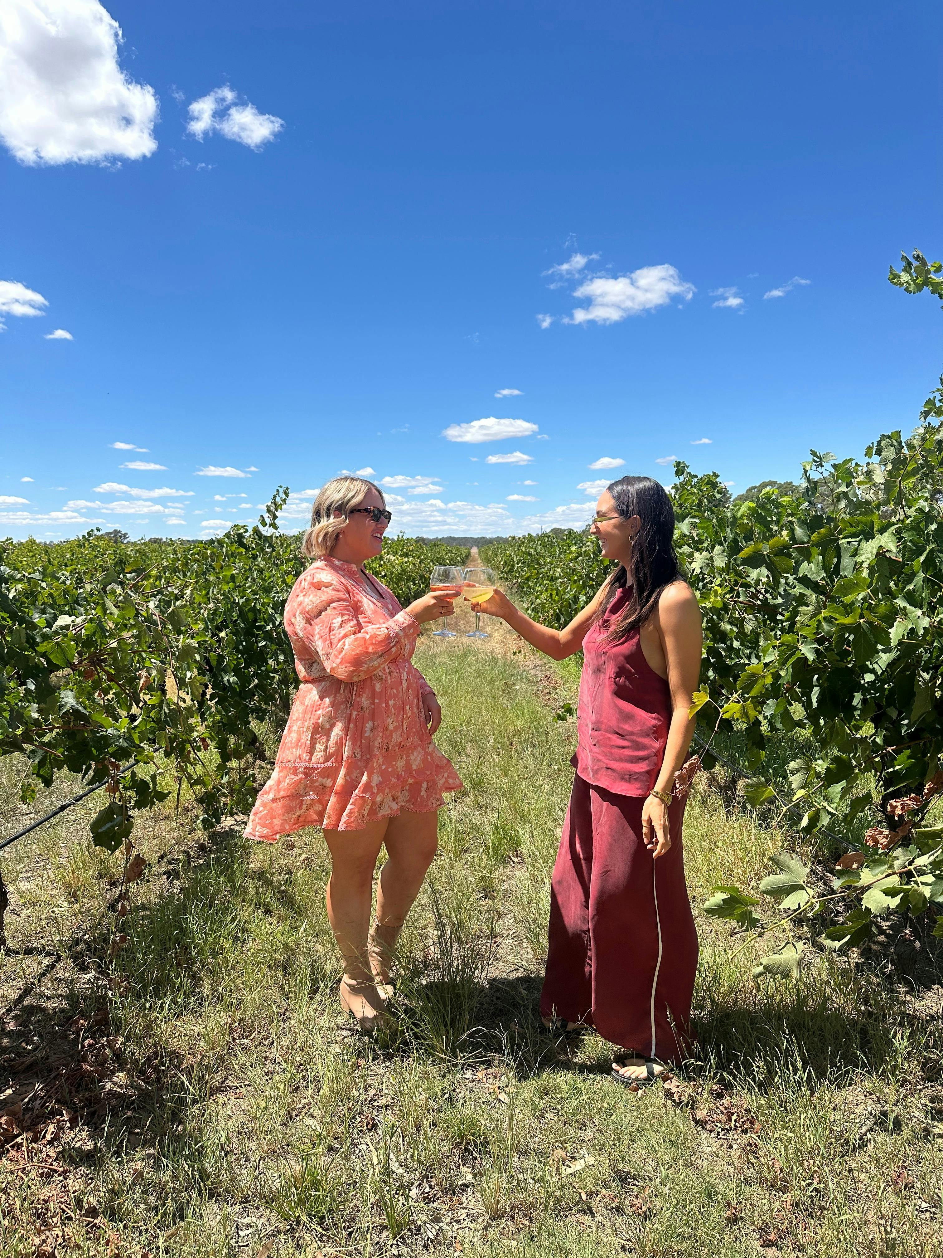 2 Women cheers while standing between grape vine