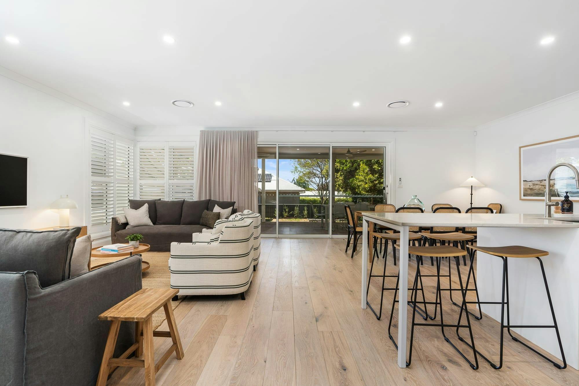 Large open living room looking out to the deck area. Modern kitchen, lounge room and dining.