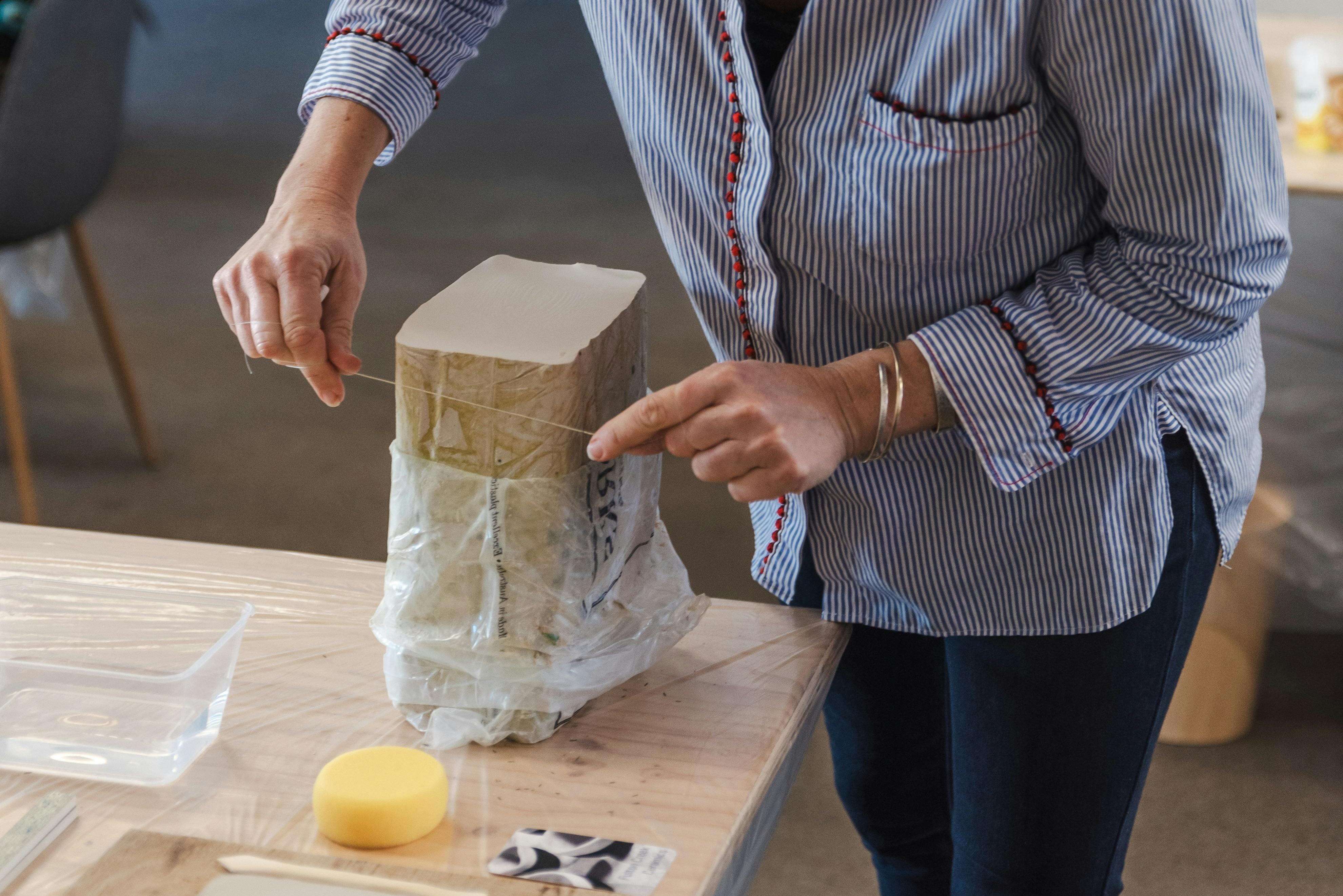 A teacher is using a wire cutter to remove a slab of fresh clay from its packet