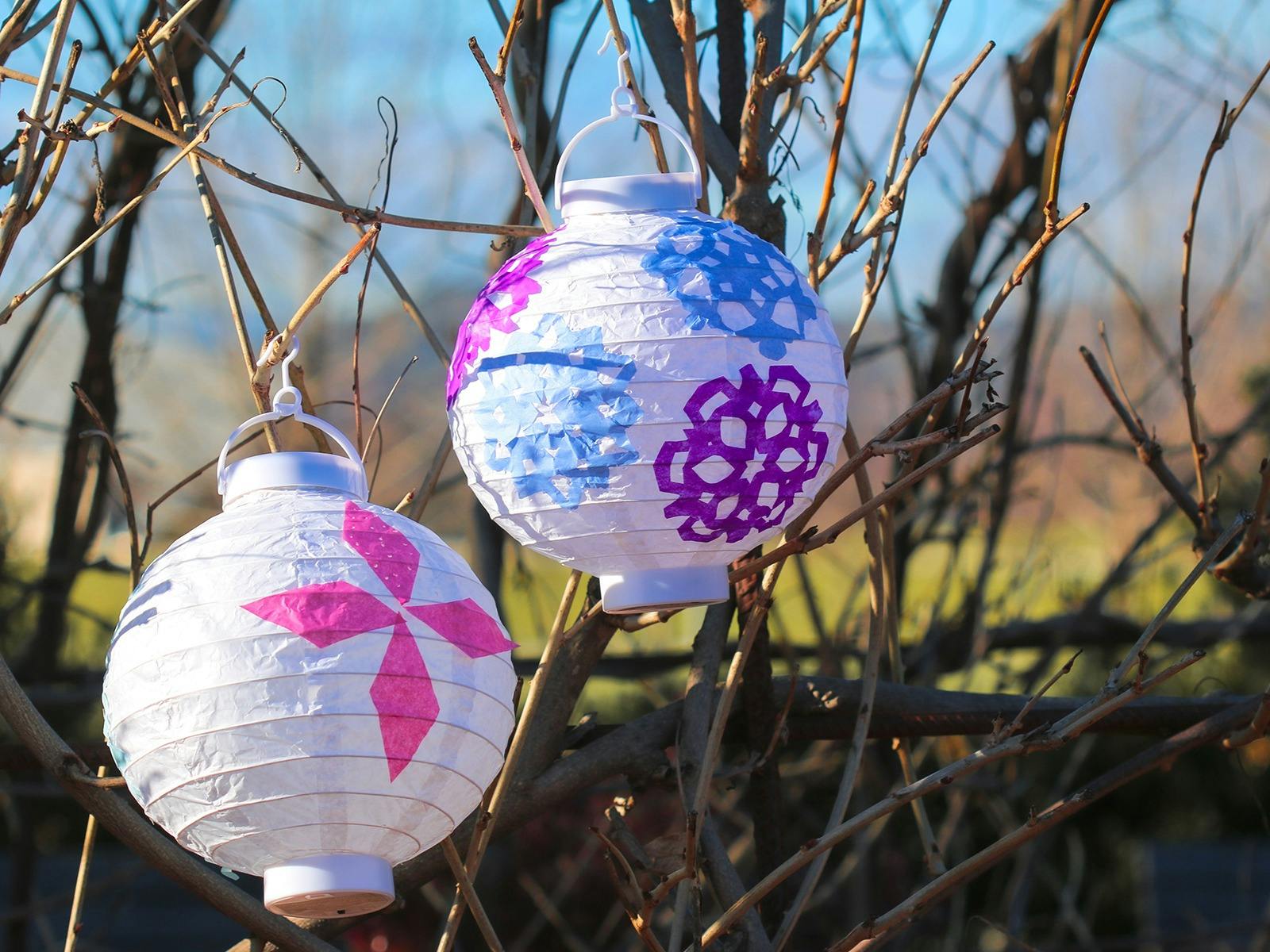two white lanterns with colourful winter cutout patterns