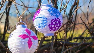 two white lanterns with colourful winter cutout patterns