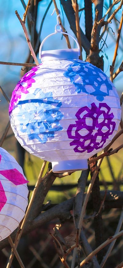 two white lanterns with colourful winter cutout patterns