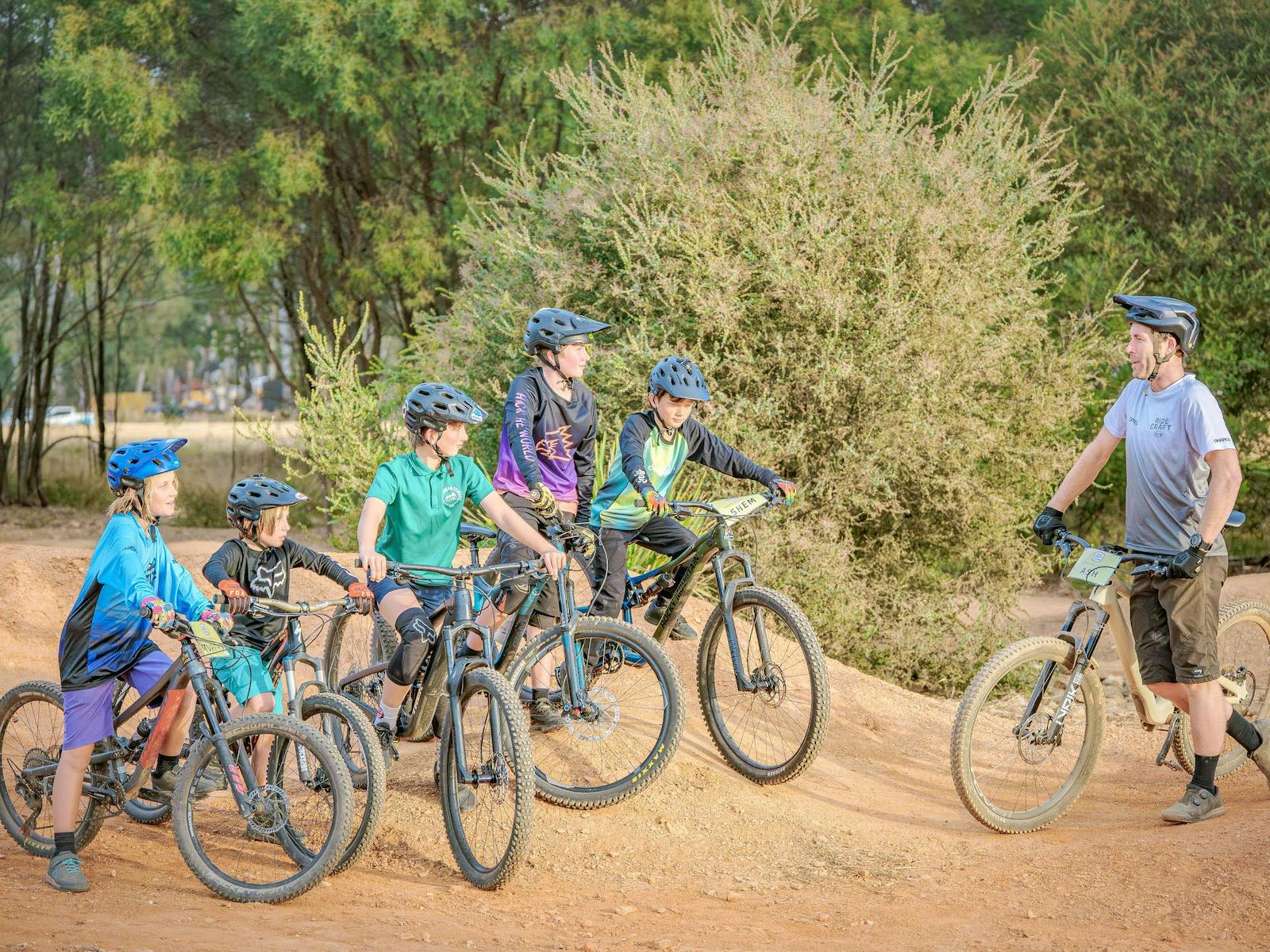 A group of kids with bikes stand with a man, also holding a bike.