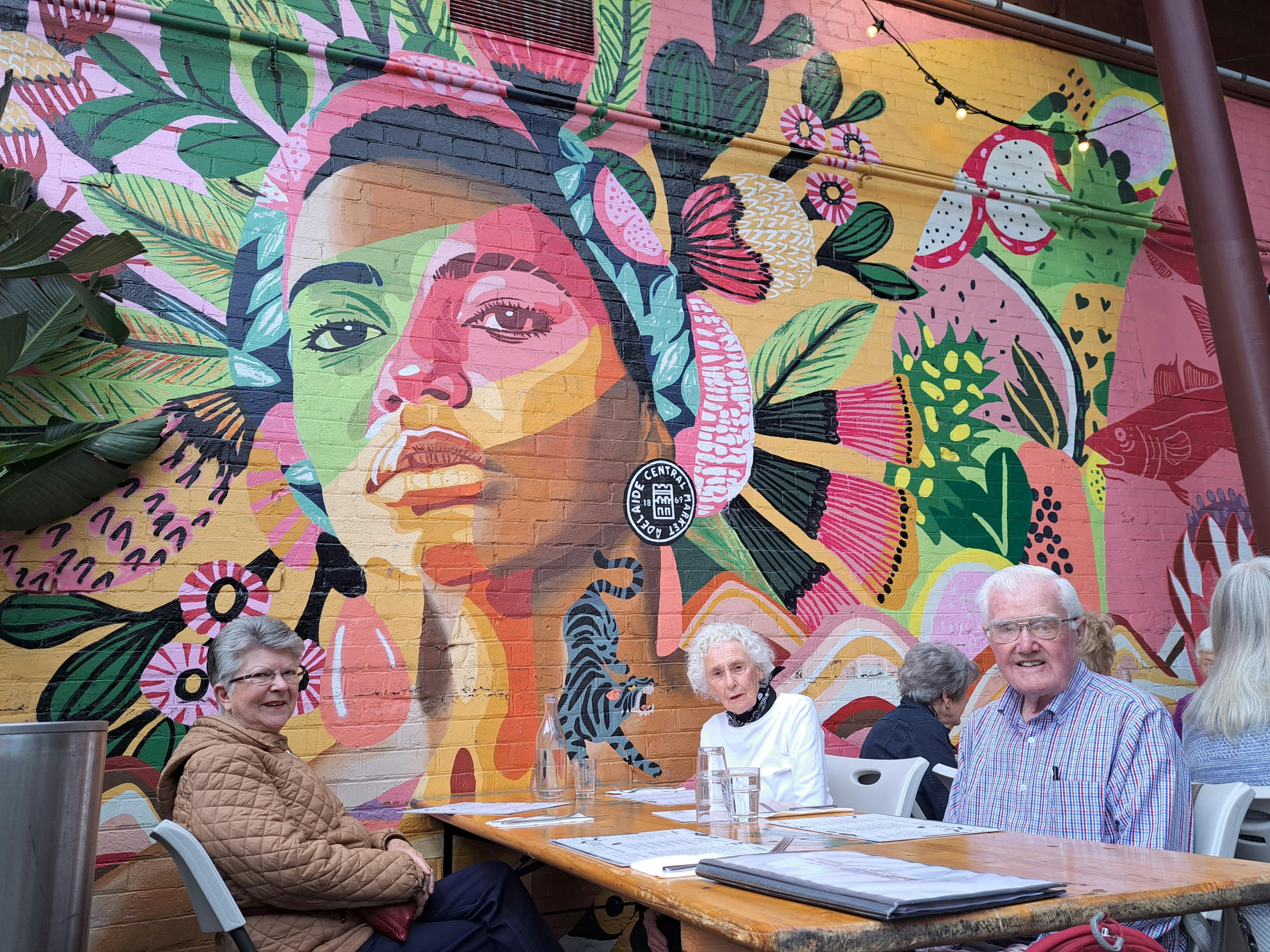 three seniors at cafe in front of colourful mural