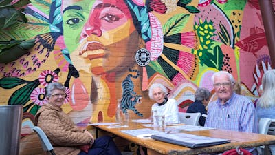 three seniors at cafe in front of colourful mural