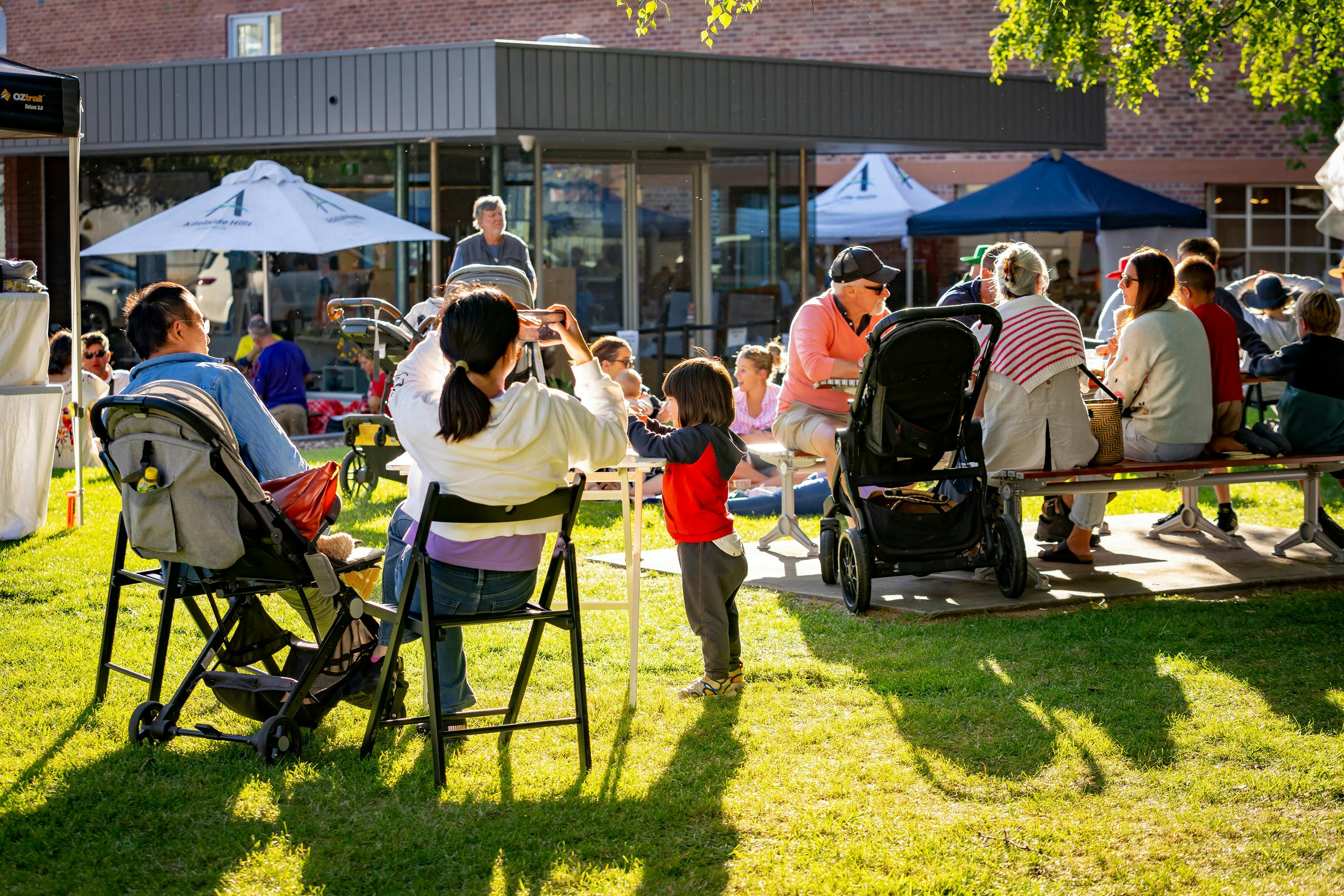 Families seated outdoors at FABRIK’s Handmade Christmas Market with prams and picnic tables