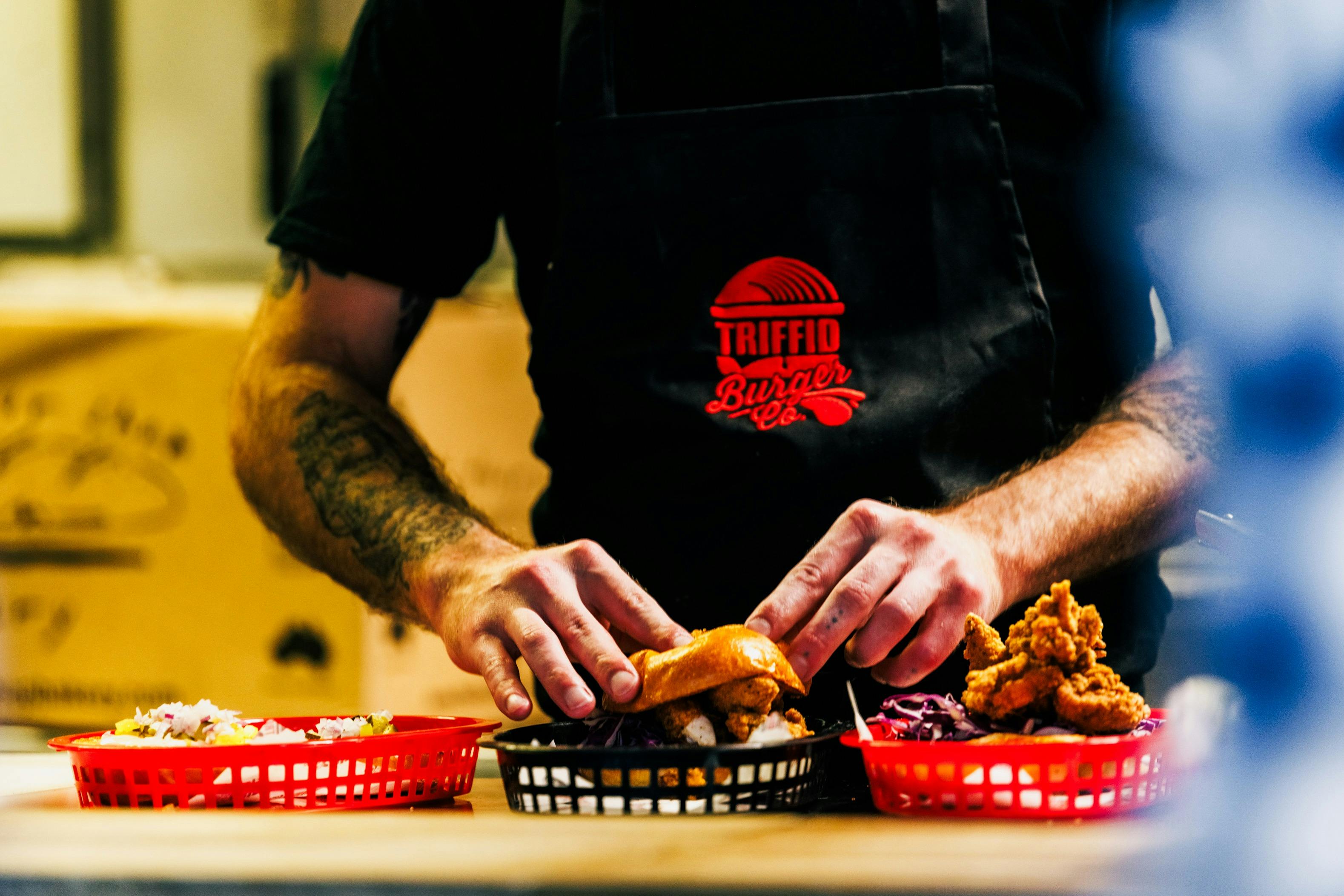 Chef putting a burger bun on top of a burger.