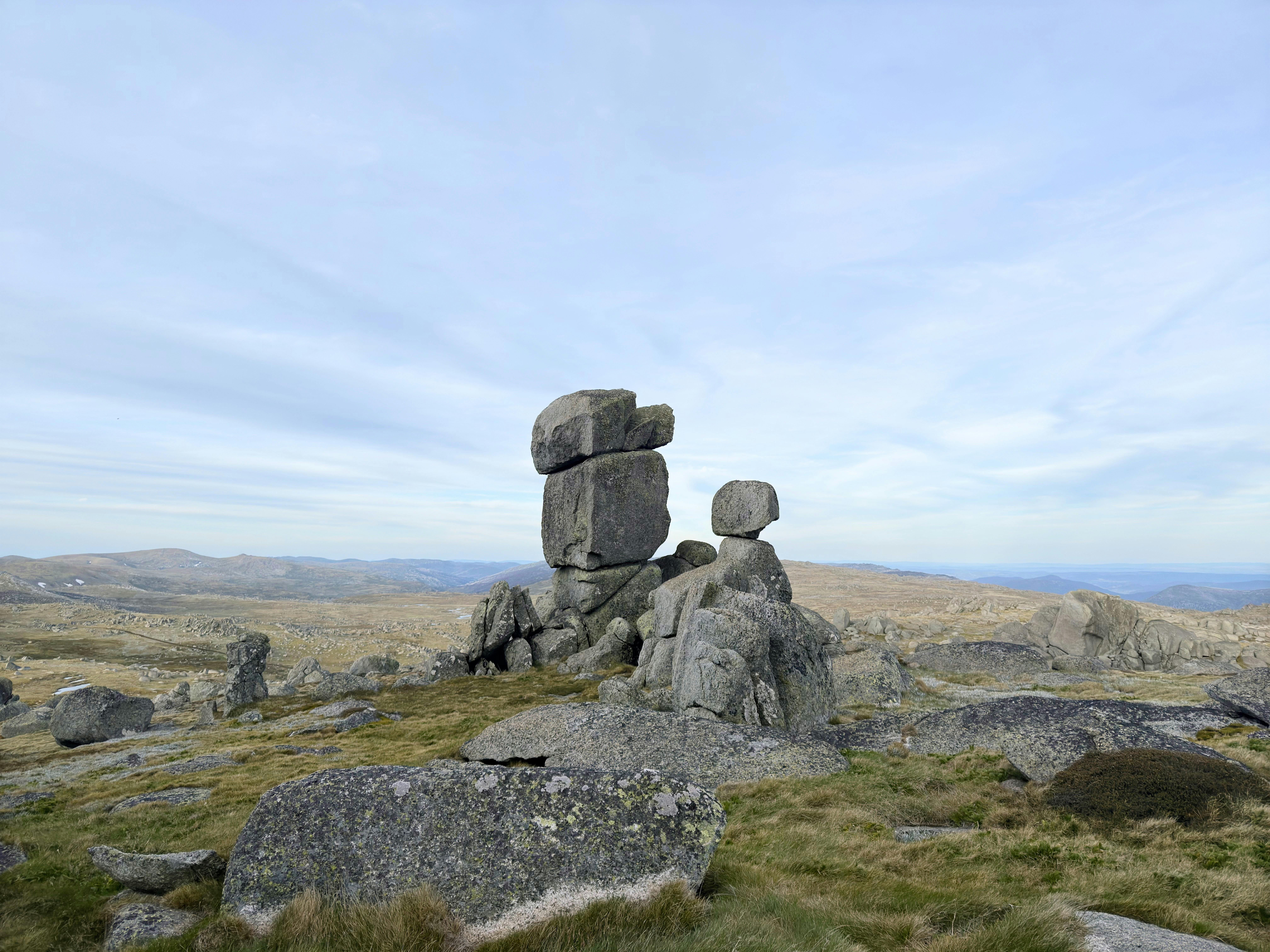 A stack of boulders in an open field in the mountains with an overcast sky.