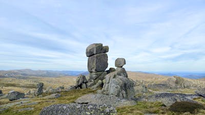 A stack of boulders in an open field in the mountains with an overcast sky.