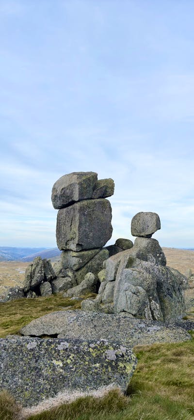 A stack of boulders in an open field in the mountains with an overcast sky.