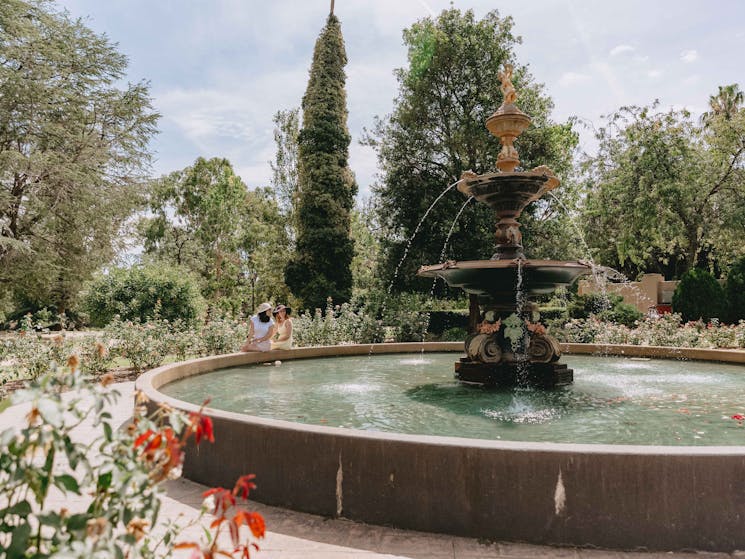 A large historic fountain centred within a pathway and bed of roses