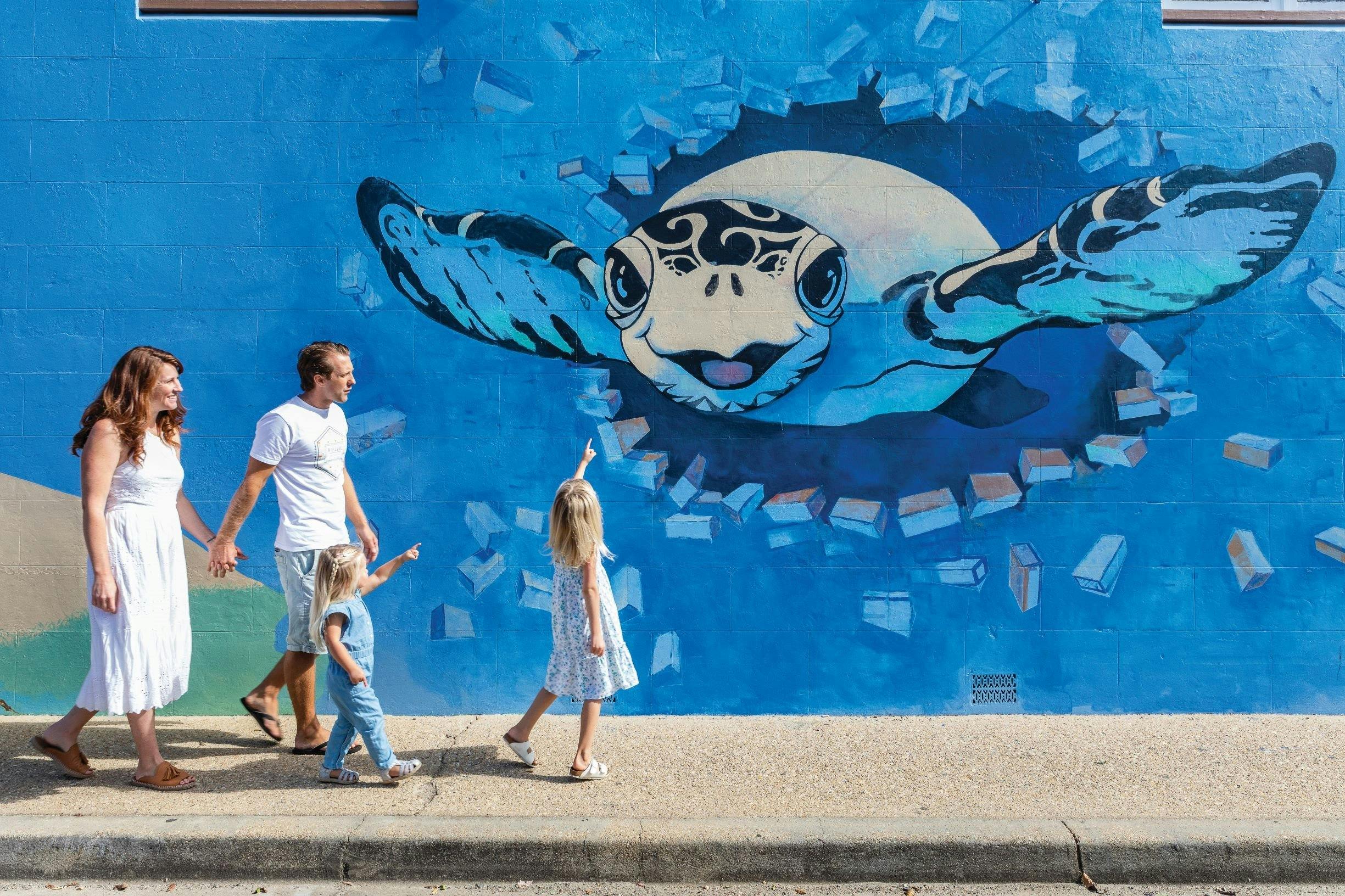 Family walking down Wallace Lane in Macksville looking at one of many colourful murals in the lanewa