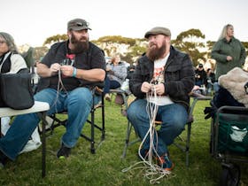 Men sitting and plaiting whips while enjoying live music