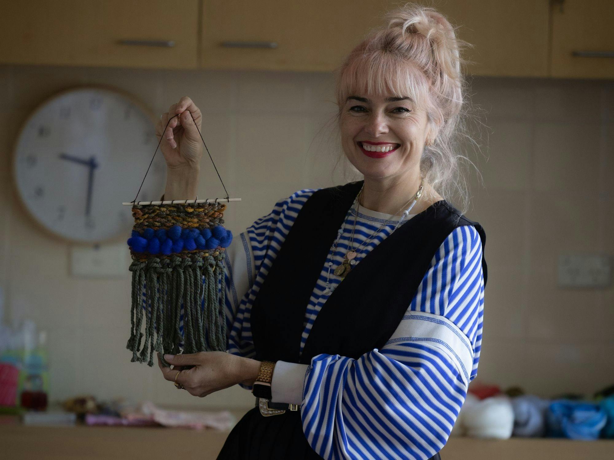 smiling woman holding up weaving art