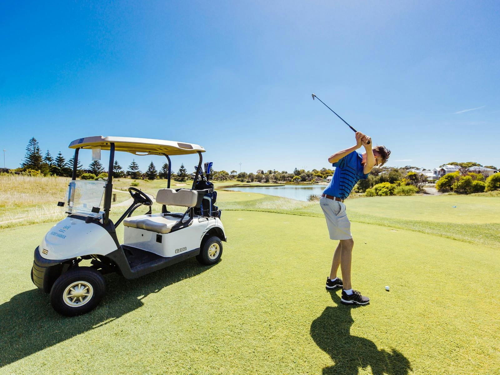 Man swinging a golf club next to golf cart
