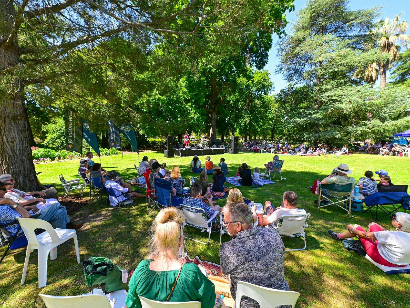 Group of people sitting on chairs and the grass in front of a stage