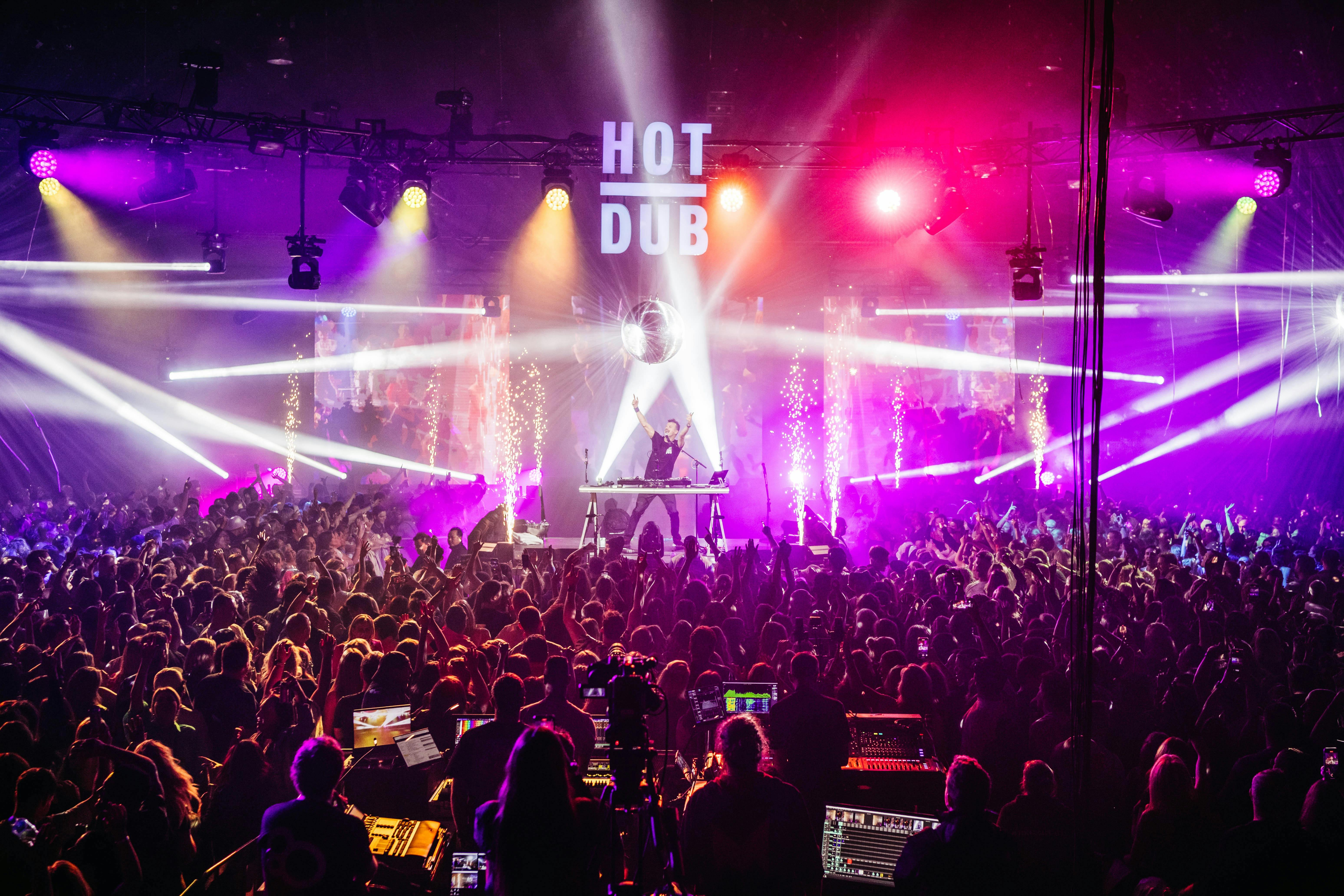 A DJ named Hot Dub Time Machine performing on stage to a large audience with colourful lights.
