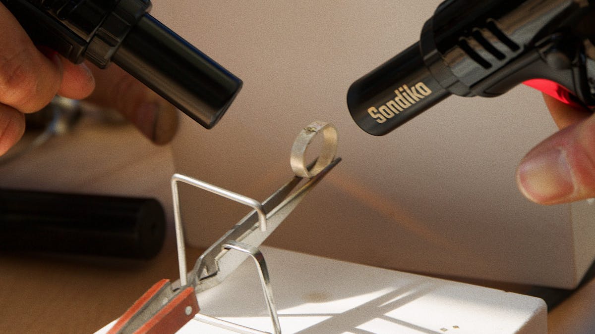 Heating silver metal with a torch, applying solder at the joint to join the ring together.