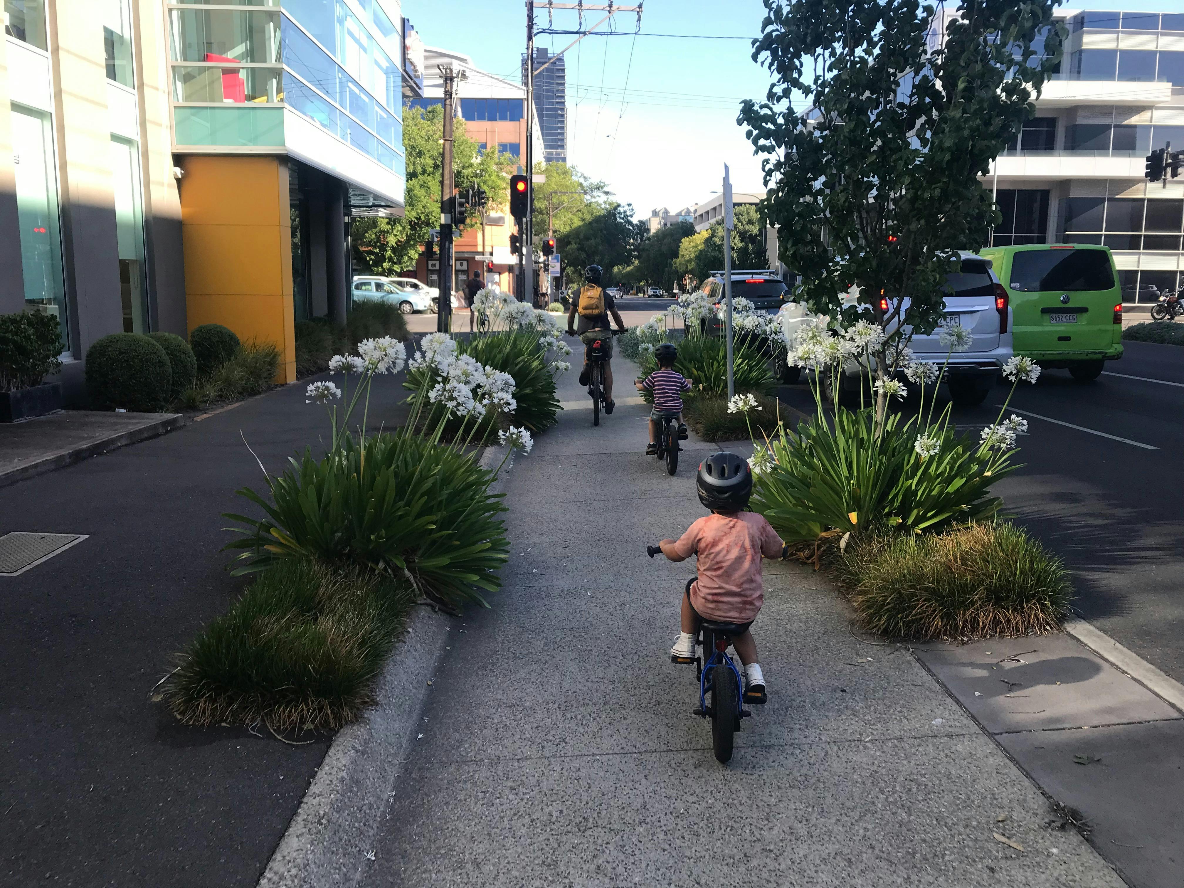 A dad and his two young sons are cycling along the protected cycle lane on Frome St