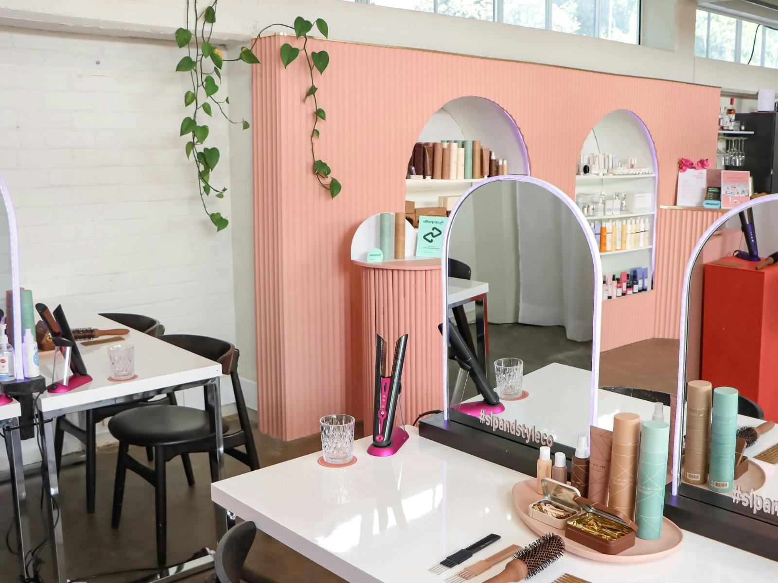Modern beauty studio with pink mirrors, styling tools, and products neatly arranged on white tables.