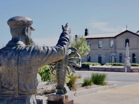 A bronze sculpture of a lobster fishermen against the backdrop of Port MacDonell's Customs House
