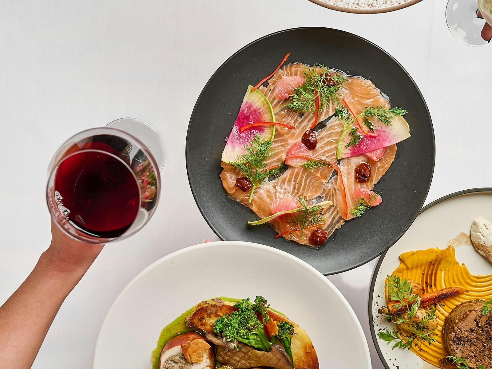 Top down view of finely plated food and a hand holding a glass of red wine