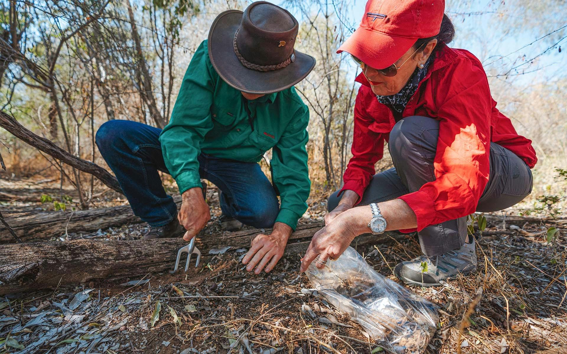 Two people digging up dirt samples from the ground for research.