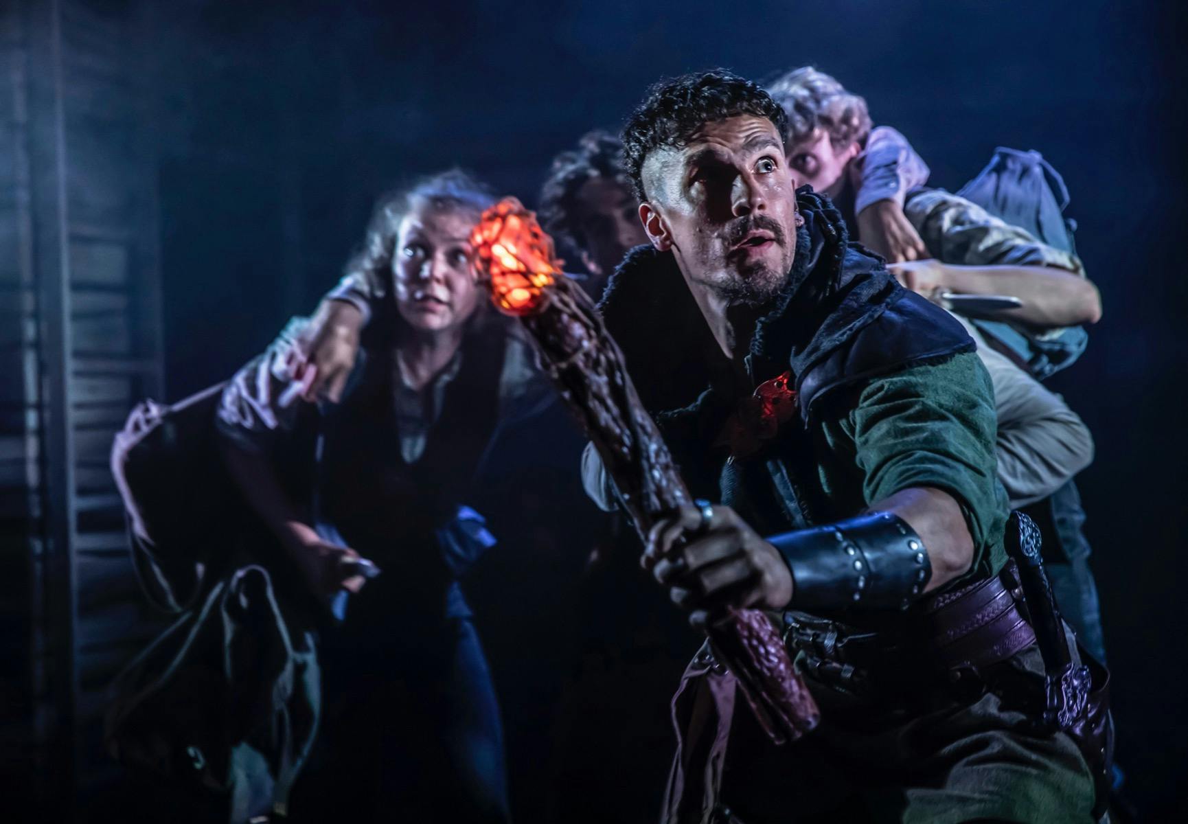 A group of Hobbits looking frightened and being led by firelight