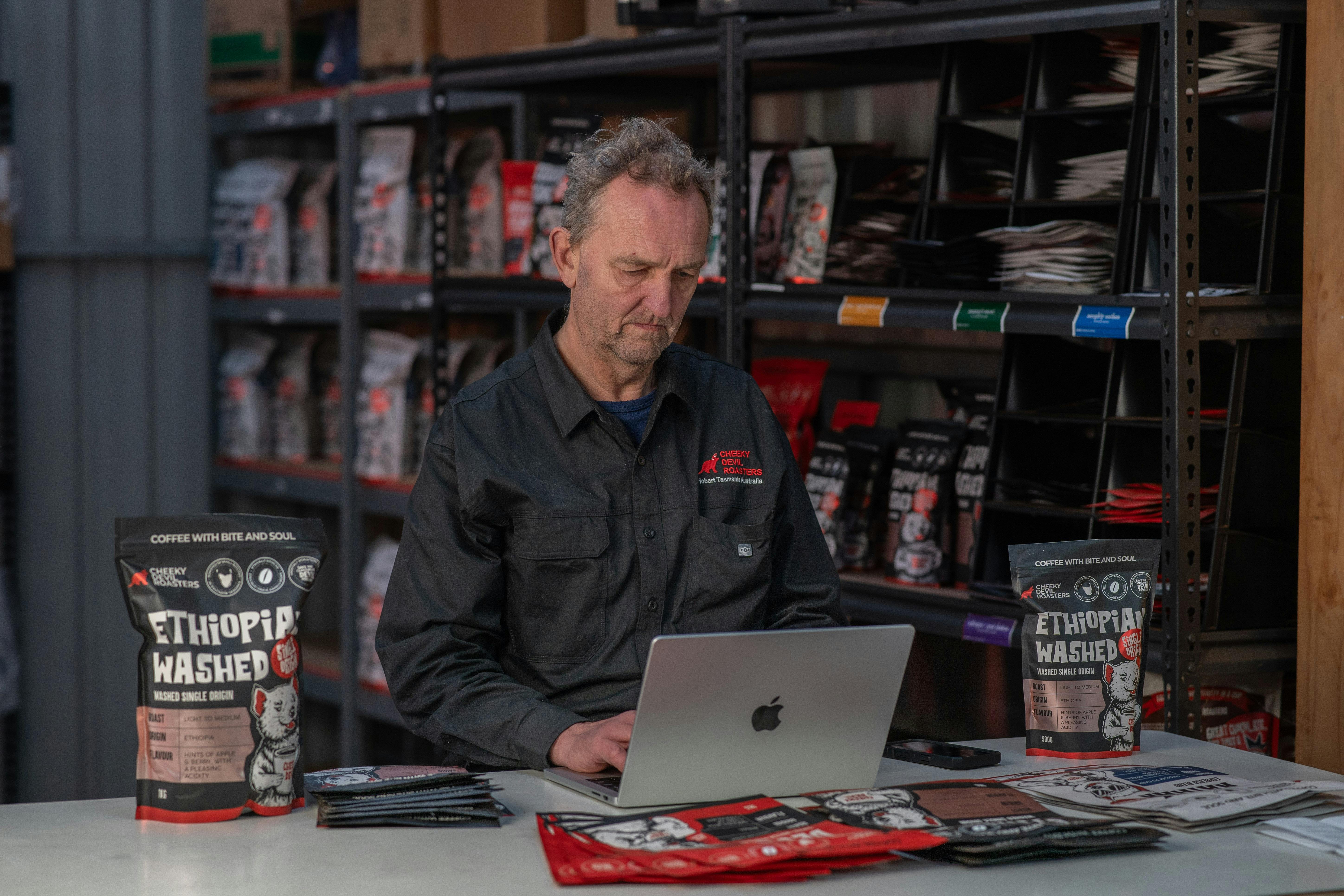 Clive Aver standing beside coffee products and roasting equipment at the Hobart roastery