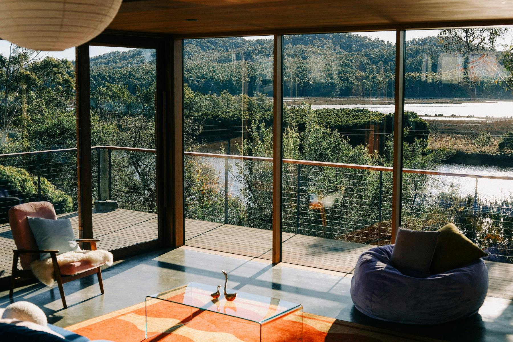 A living room with a red and yellow rug, purple bean, and floor to ceiling windows overlooking river