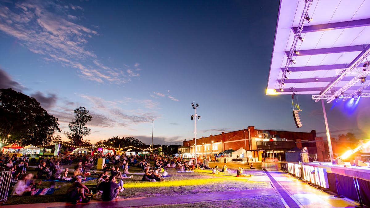 People sitting on grass with butter factory building in the background.