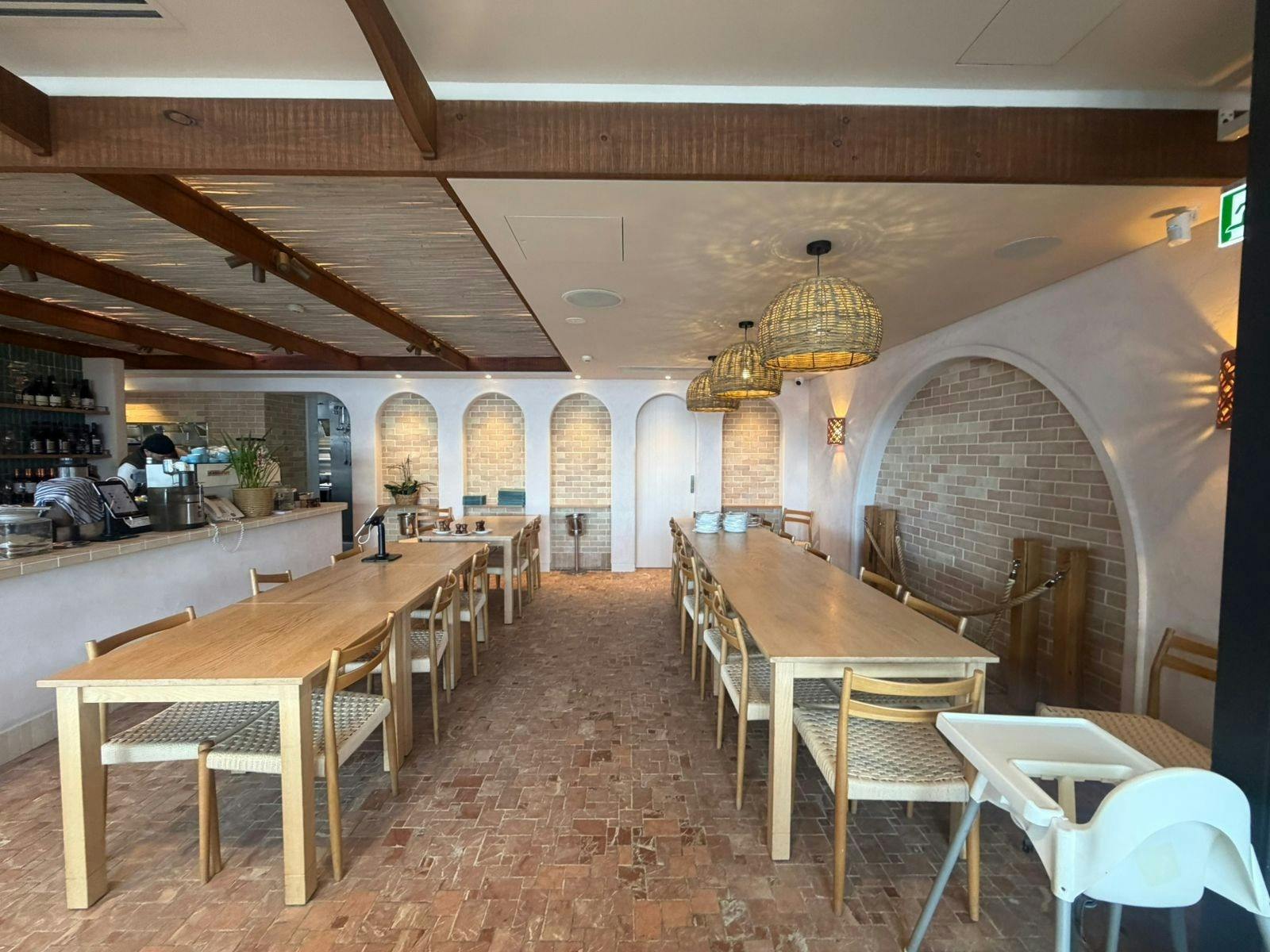 Long timber tables and woven pendant lights under brick arches in the dining room.