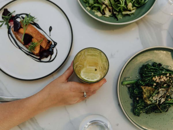 Top-down image of and holding a cocktail around plates of food.