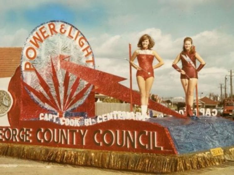 Historical photo of a float with two women dressed in red on it with St George County Council
