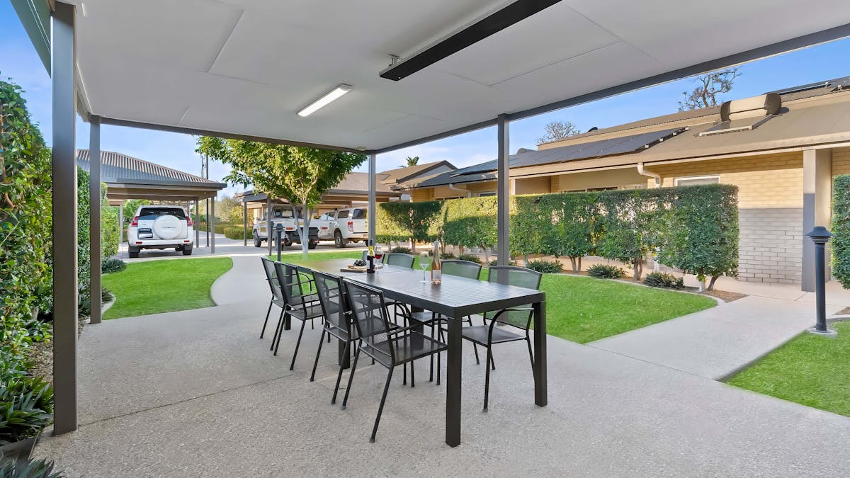 The guest BBQ area featuring an overcover dining table and grass area.
