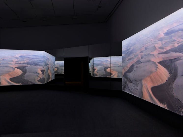 Multiple screens in dark room showing an image of mountains. From Doug Aitken: New Era.