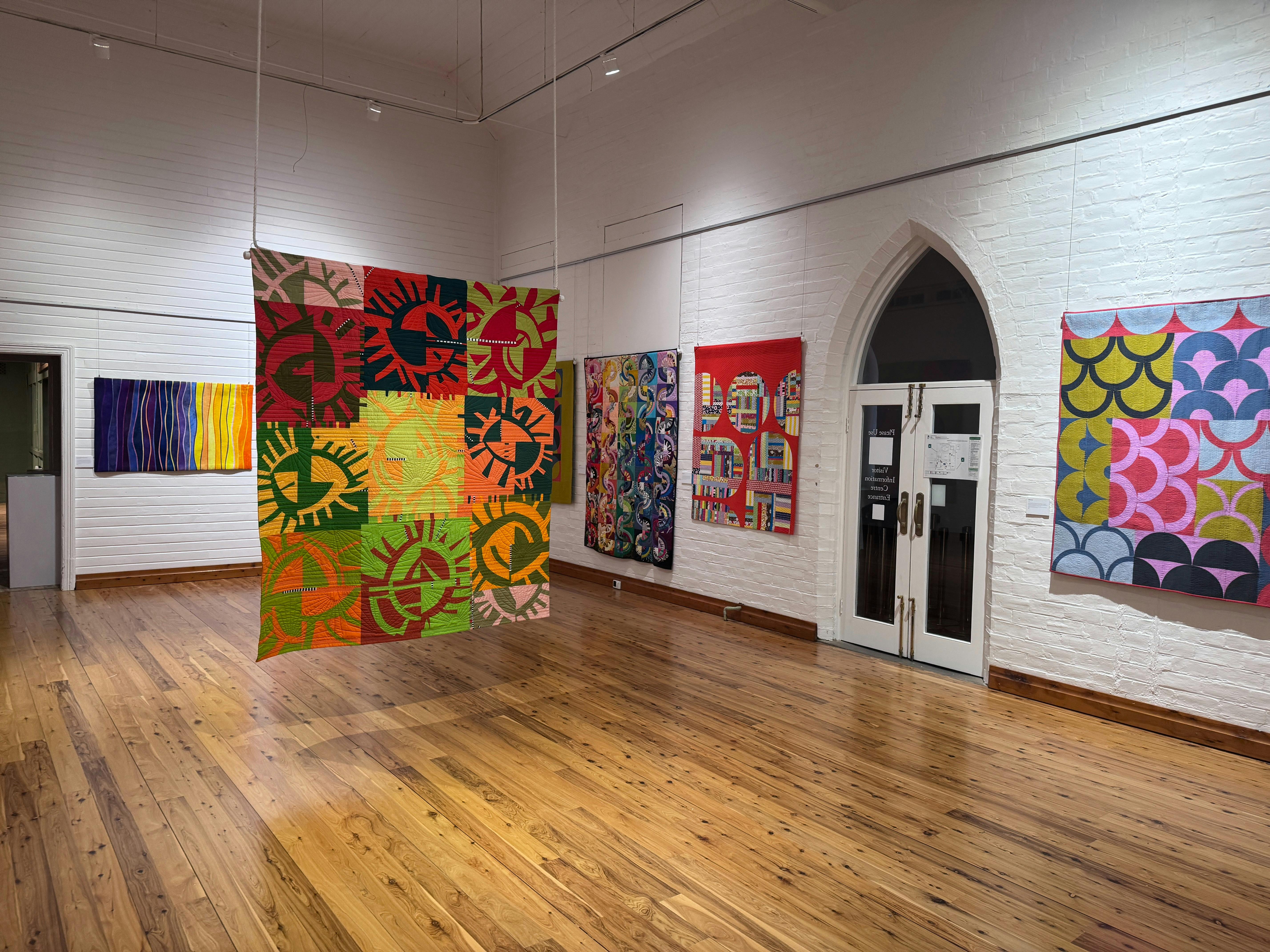 Bunte Quilts hängen von den Wänden und der Decke einer Galerie.