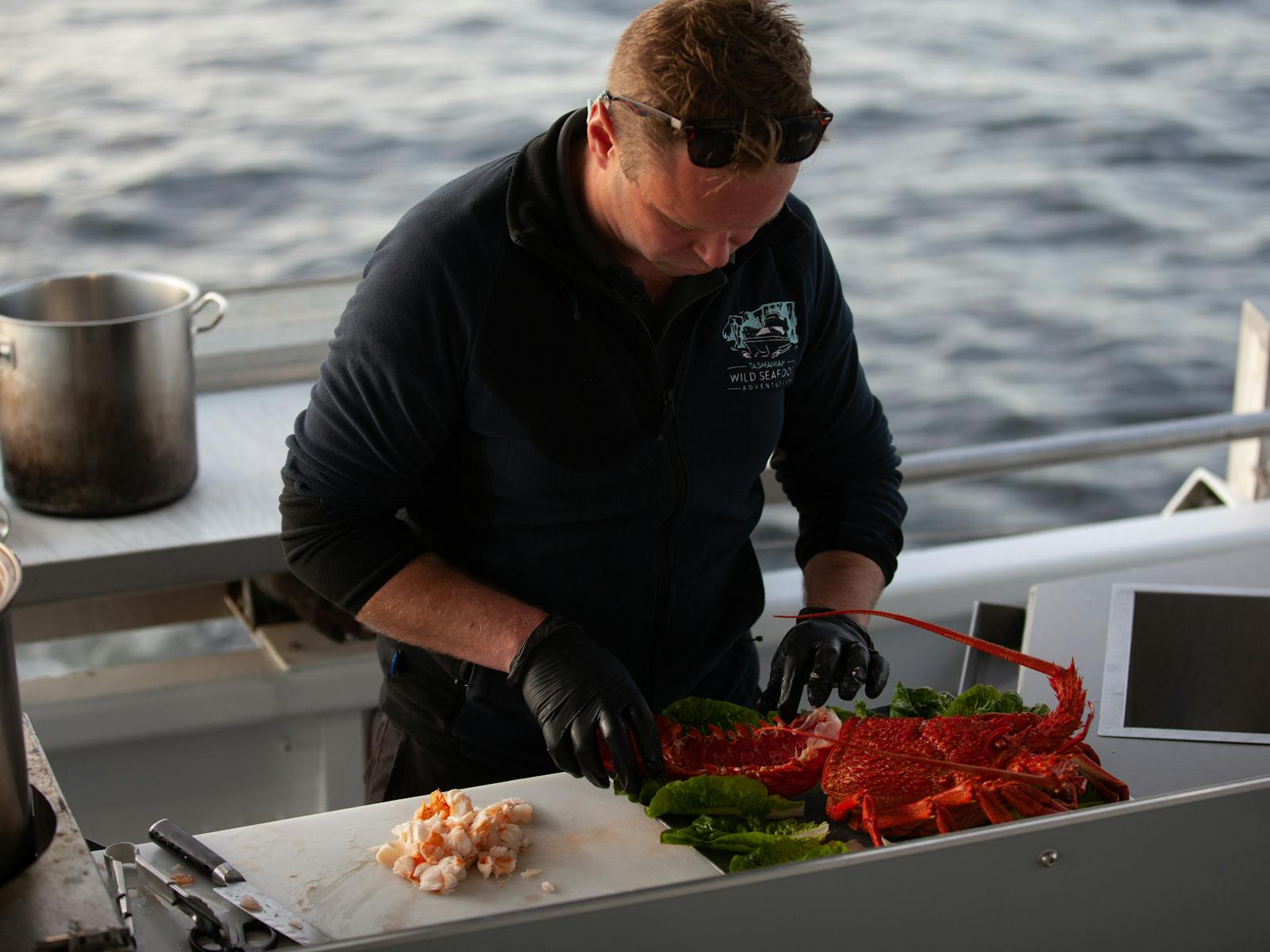 Shane prepares a recently caught Tasmanian rock lobster at the rear of the vessel with ocean behind.