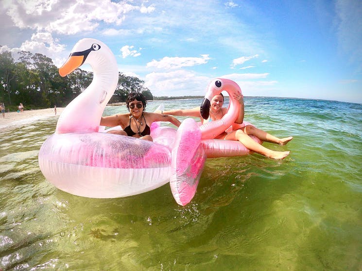 Two girls on inflatable swans / flamingos in the water at Jervis Bay