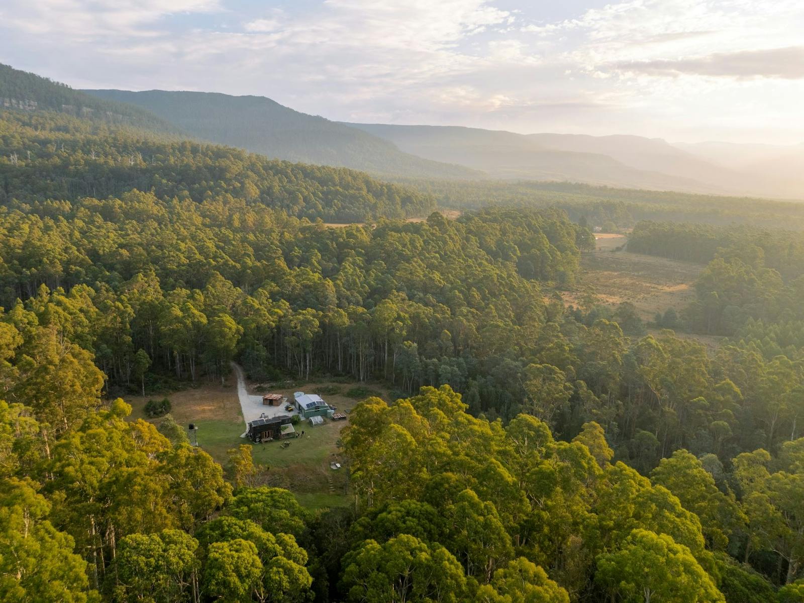 Aerial view of a secluded property nestled within dense forest at the base of a mountain range.