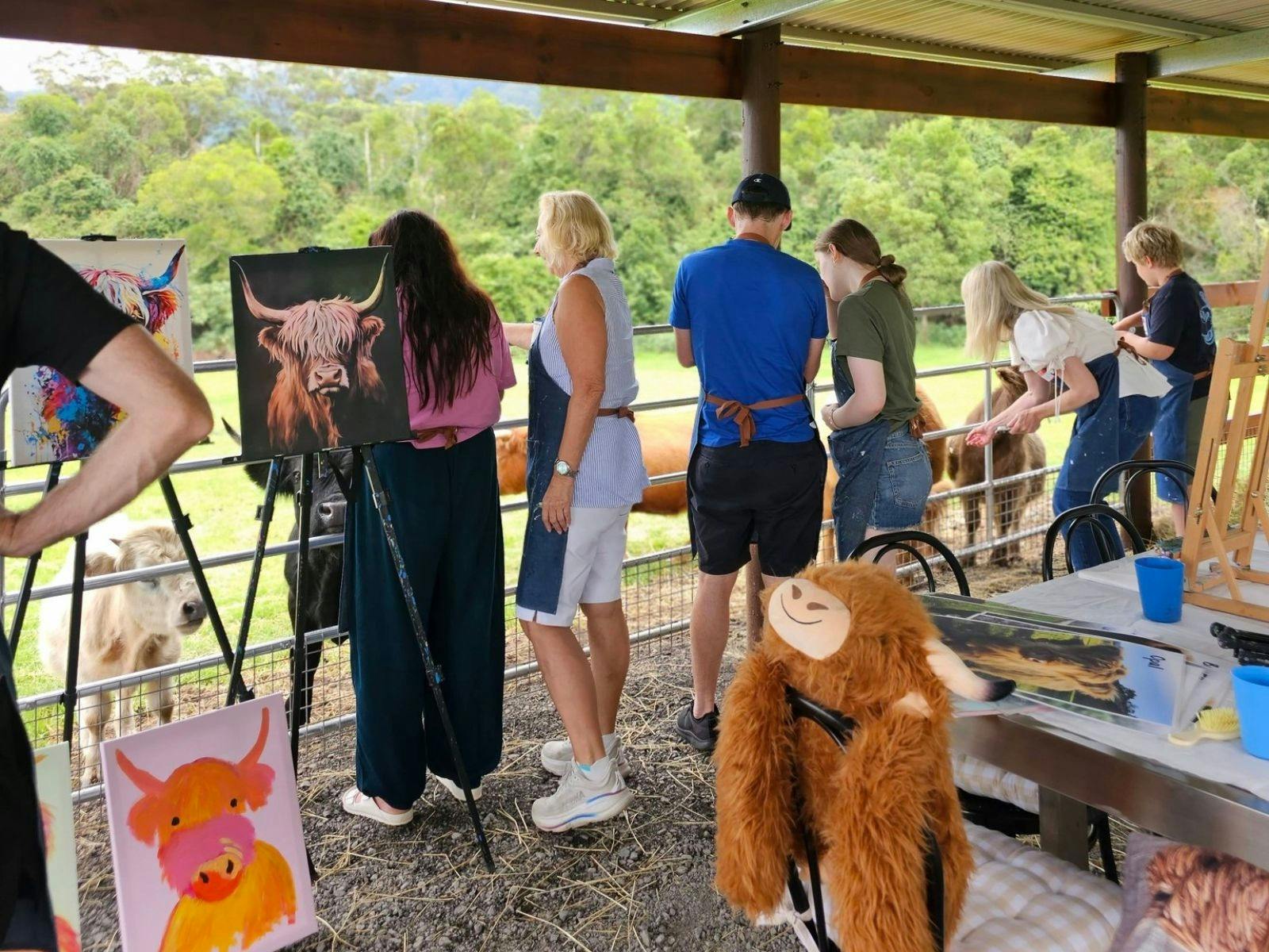 Group feeding Highland Cows surrounded by easels and wearing aprons ready to paint cows on canvas