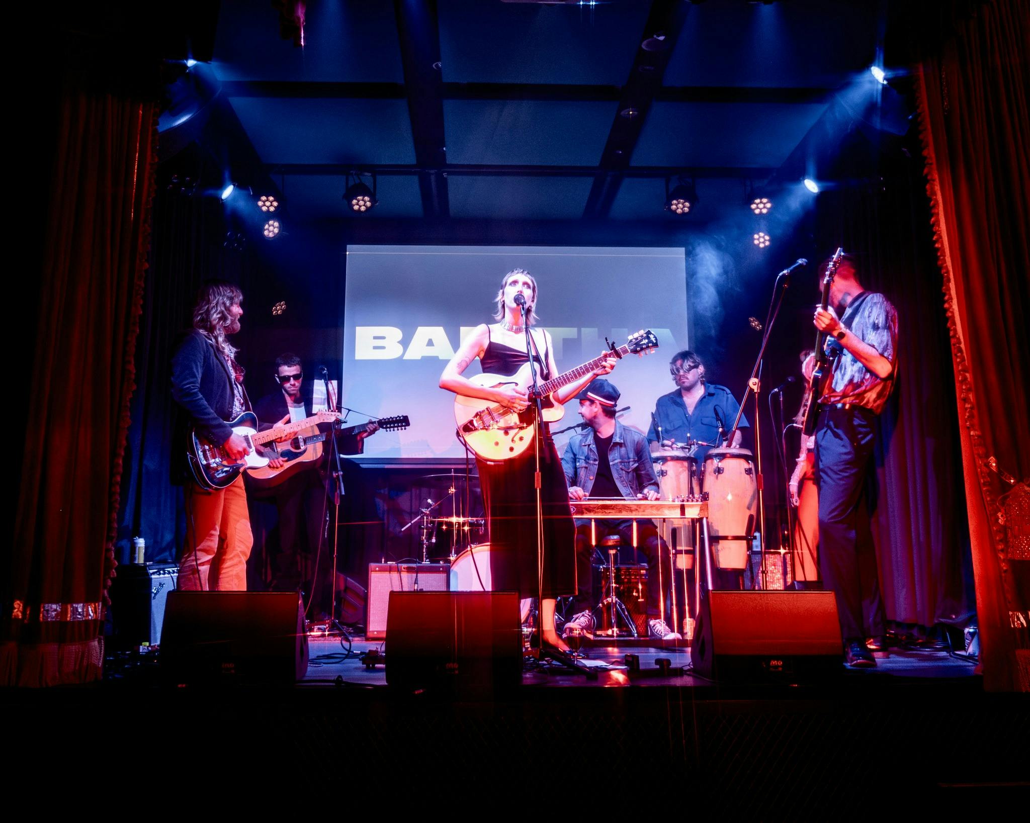 Babitha the band playing on stage surrounded by red curtains
