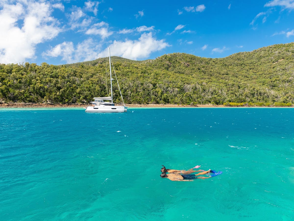 Person snorkelling in turquoise waters close to a sailing boat that is moored at a Hook Island bay