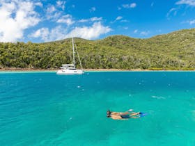 Person snorkelling in turquoise waters close to a sailing boat that is moored at a Hook Island bay
