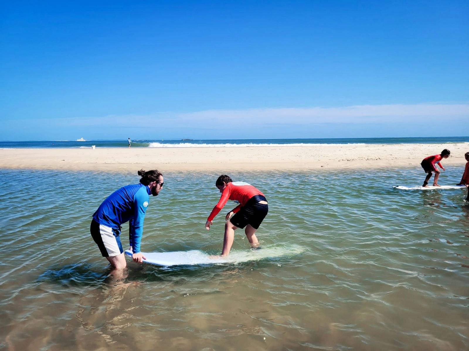 AAC staff assisting a young person to balance on a surfboard in the water