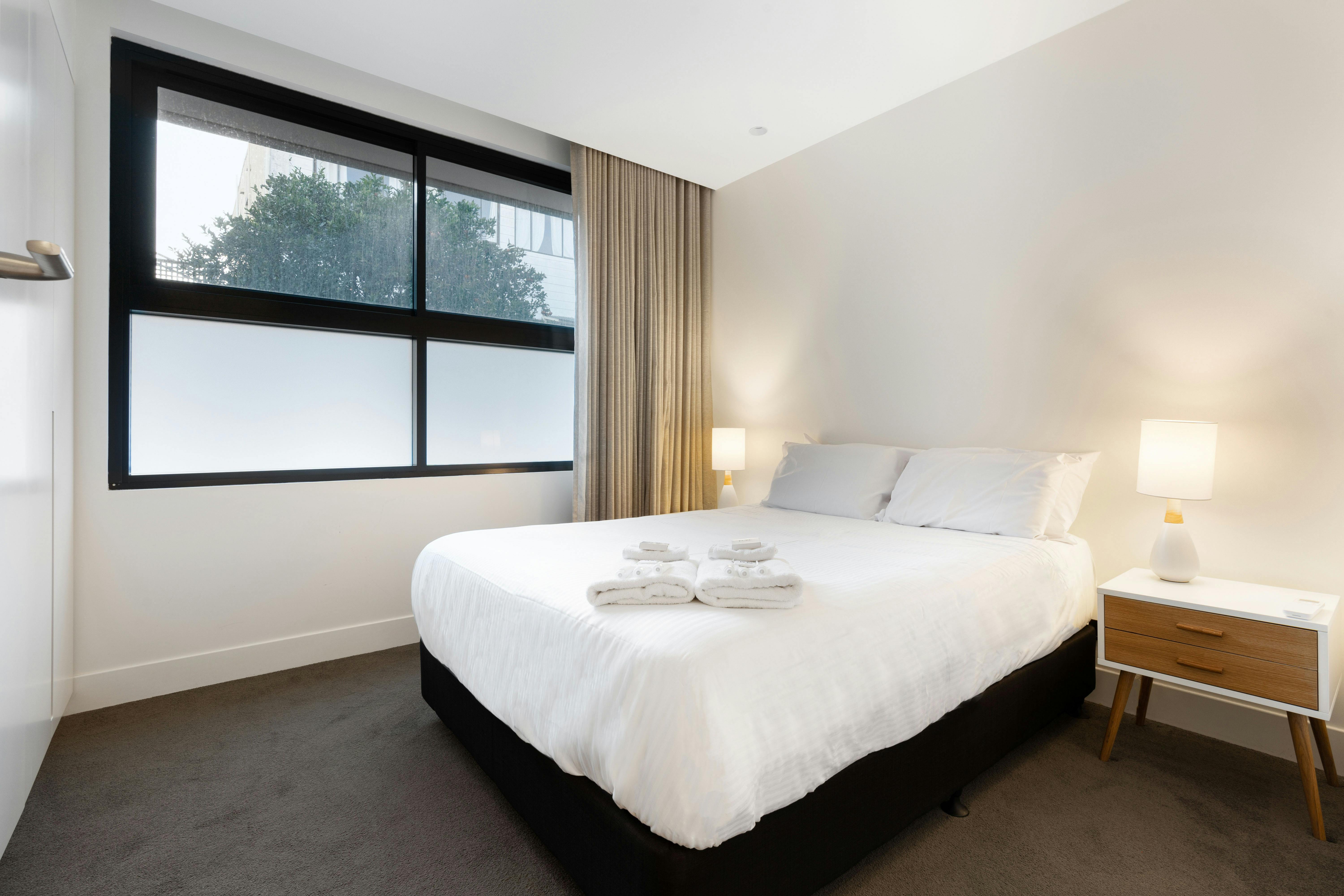 Cozy bedroom with natural light, stylish bed, and warm lamps.
