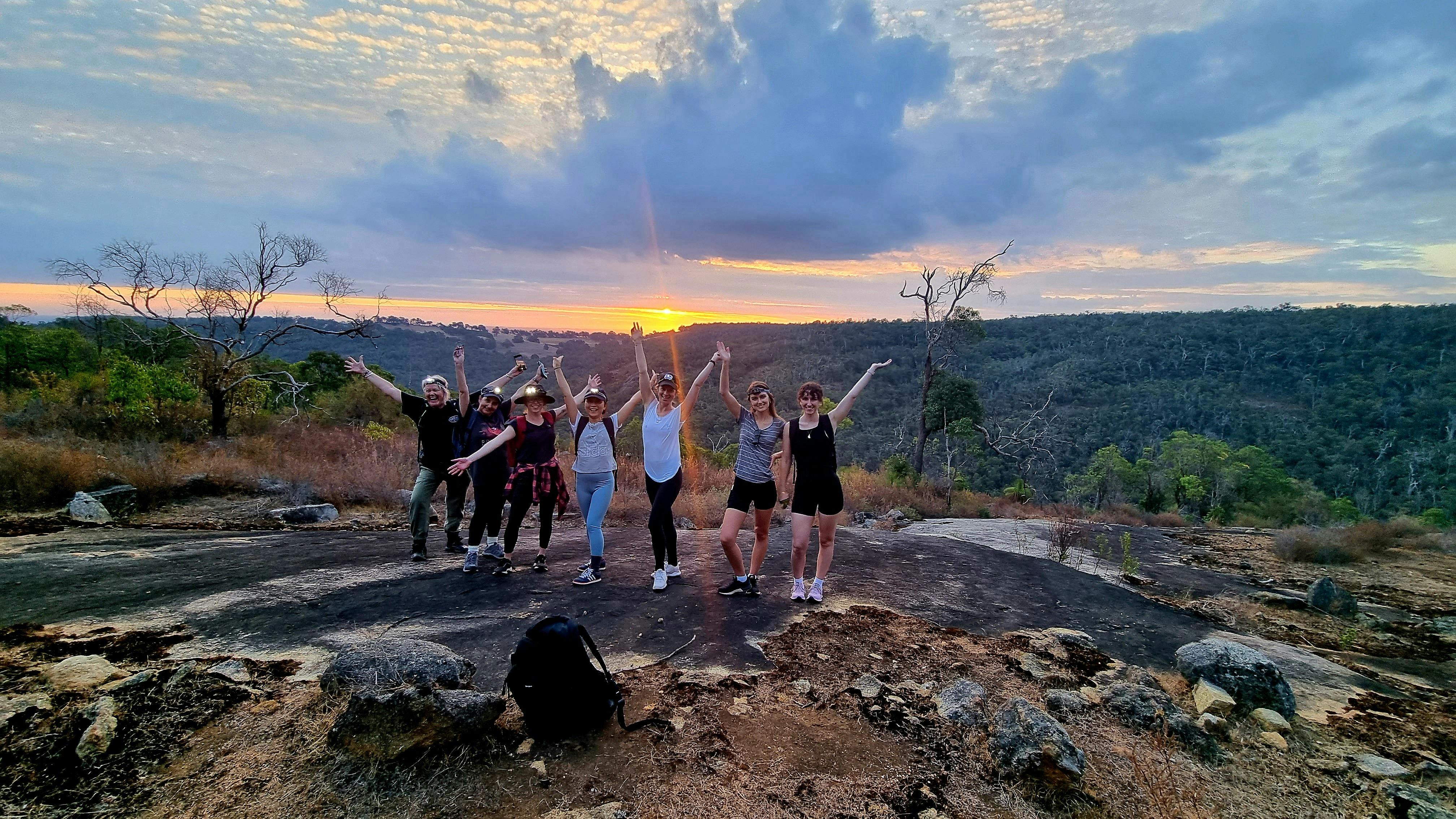 hikers standing on granite rock screaming woohoo with sunset in background